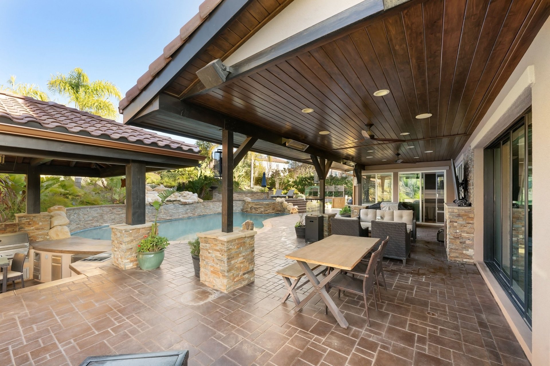 Luxury outdoor living space with covered patio, pool, lush landscaping, and stone accents