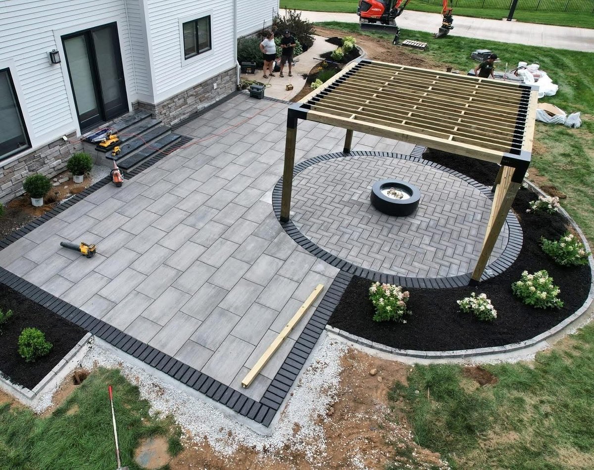 Aerial view of a modern backyard patio with gray pavers, pergola, fire pit seating area, and landscaping