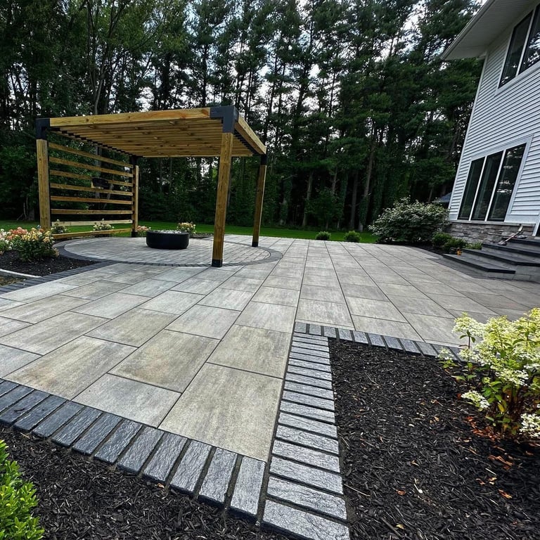 Modern backyard patio with gray pavers, wooden pergola, and landscaped gardens