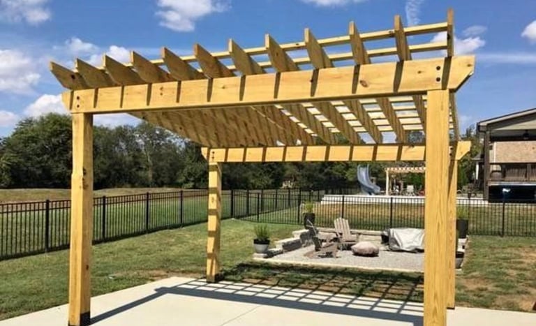 Yellow wooden pergola structure over patio seating area with fire pit in backyard garden setting
