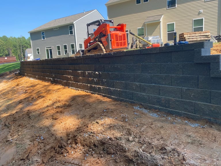 Red equipment on truck behind black retaining wall with residential houses in background